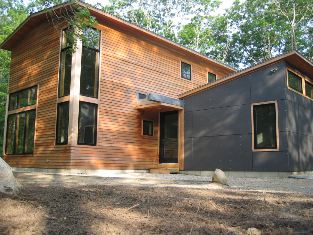Modern home exterior with a shed roofline, cedar entry, and charcoal panel siding among the trees