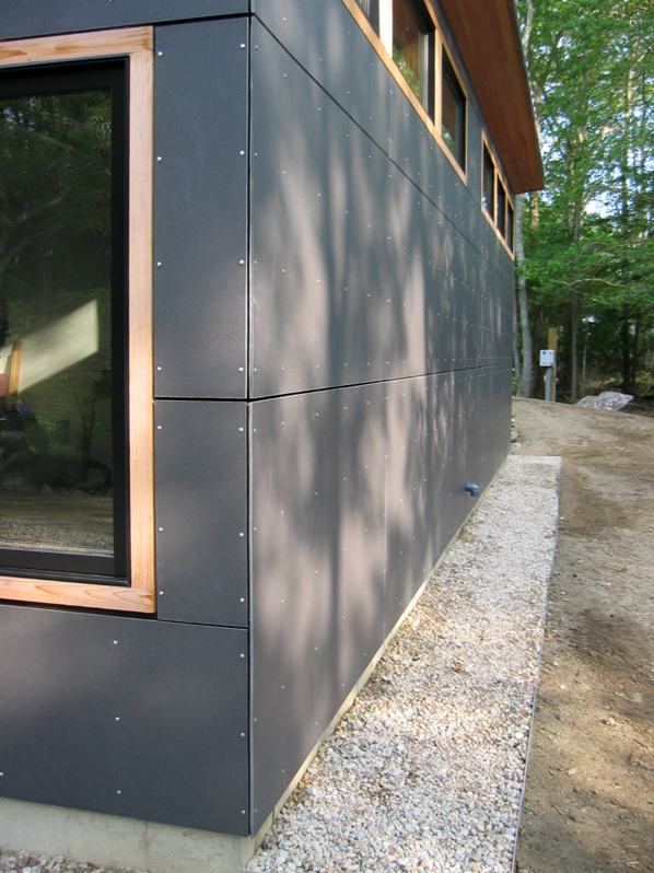 Detail of charcoal fiber-cement panel seams beside a cedar-framed window