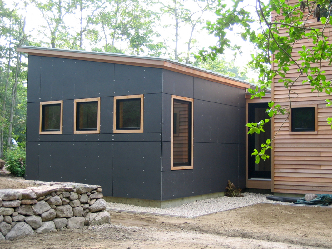 Modern home exterior with charcoal fiber-cement panel and cedar siding, viewed from a stone retaining wall
